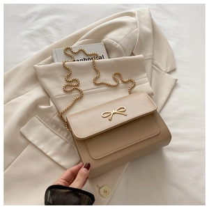 Détail du sac à rabat beige avec fermoir en forme de nœud doré et bandoulière chaîne