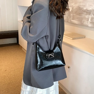 Glossy black shoulder bag with silver bow accent shown on model for size and style