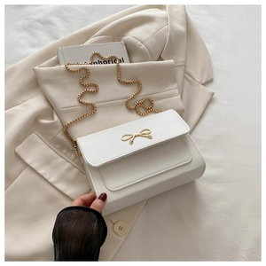 Détail d'un sac en cuir blanc avec fermoir nœud doré et bandoulière en chaîne élégante