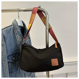 Detail of black canvas crossbody bag with vibrant colorful striped wide shoulder strap