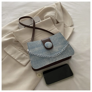 Detail of blue denim fabric texture and brown leather strap on a stylish crossbody bag
