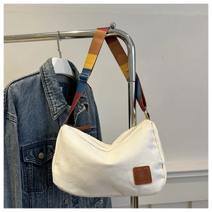 Detail view of off-white canvas hobo bag featuring colorful striped shoulder strap