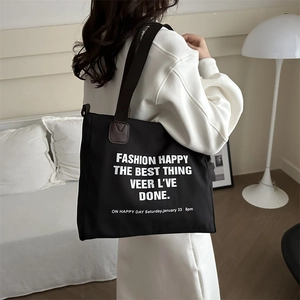 Grand sac cabas noir en toile avec lettres blanches et anses en cuir porté à l'épaule