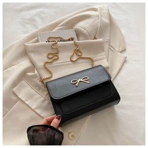 Détail d'un sac en cuir noir avec fermoir nœud doré et chaîne à billes sur blazer beige