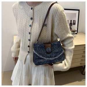 Détail du sac sous le bras en denim vintage avec rabat en cuir brun et chaîne argentée