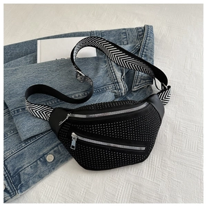 Detail of black waist bag with studs and wide geometric strap on denim background