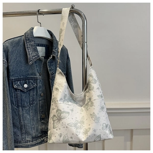 Close-up of white canvas tote bag with vintage green butterfly prints on a metal hanger
