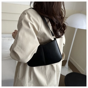 Detail of minimalist black leather shoulder bag with gold buckle on a model