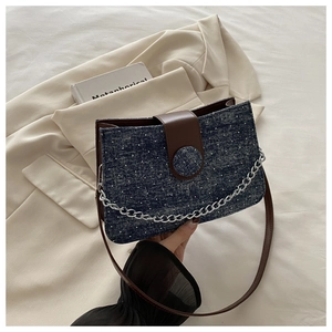 Detail of dark blue denim crossbody bag with silver chain on beige blazer background