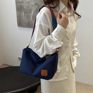 Navy canvas dumpling bag featuring colorful woven shoulder strap and brown leather patch