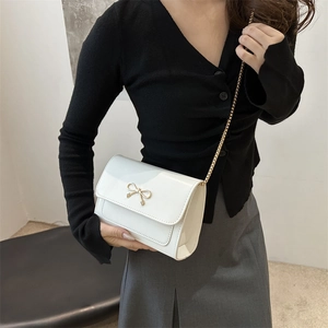 Sac bandoulière blanc élégant avec fermoir nœud doré et bandoulière chaîne sur modèle