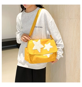 Detail of yellow nylon messenger bag featuring white plush star patches and wide strap