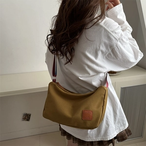 Canvas crescent shoulder bag in mustard yellow with colorful striped straps on model