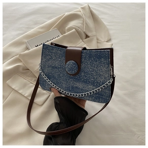 Close-up of denim shoulder bag with white polka dots, brown leather flap and silver chain