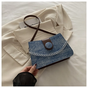 Detail of blue denim crossbody bag with brown leather flap and silver metal chain strap