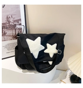 Close-up of black messenger bag with white plush stars on a minimalist display stand