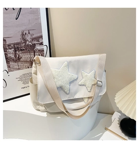 Detail of white canvas messenger bag featuring plush yellow stars and wide shoulder strap