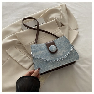 Detail of denim crossbody bag with silver chain strap and leather strap on beige blazer