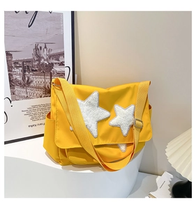 Detail of yellow nylon messenger bag featuring white plush star patches on a display stand