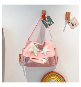 Detailed close-up of pink messenger bag with white plush stars on a minimalist wall hook