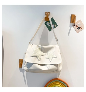 Detailed view of white canvas messenger bag with cute beige plush star patches on white wall