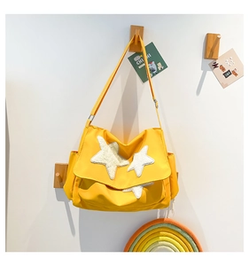 Detail of yellow messenger bag with plush stars and adjustable strap on white wall