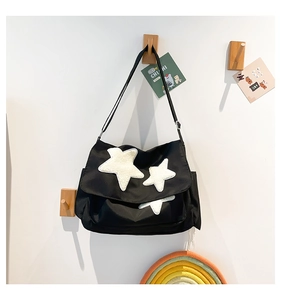 Detail of black messenger bag with star patches hanging on a wooden wall hook