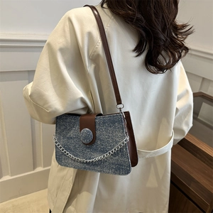 Blue denim crossbody bag with brown leather flap and silver chain on beige coat