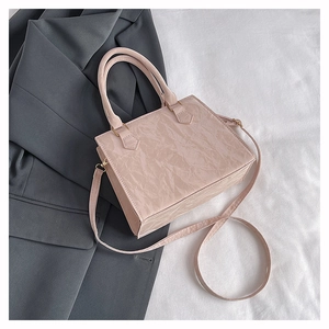 Detailed view of pink pleated PU leather crossbody bag with gold hardware on grey suit