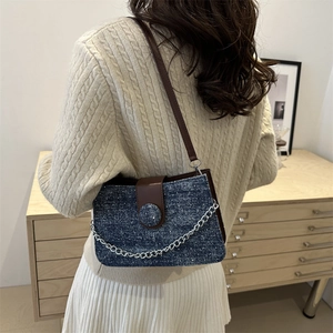 Blue denim crossbody bag with brown leather strap and silver chain on model in cozy room