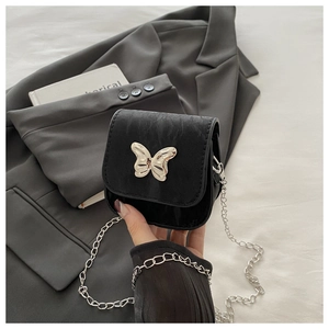 Detail van een mini zwarte crossbody tas met een gouden vlindersluiting en metalen ketting