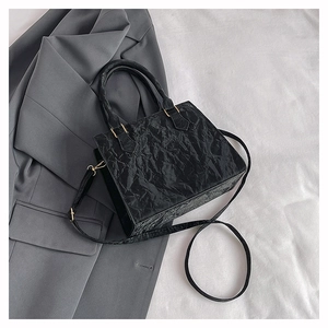 Detail of black pleated PU leather square bag with golden hardware and shoulder strap