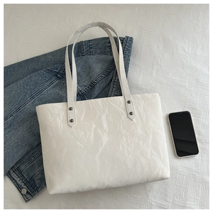 Detail showing white crinkle leather texture and sturdy rivet straps on a large tote bag