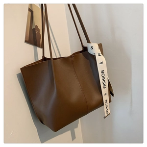 Detail of a brown matte leather tote bag featuring a decorative FASHION ribbon strap