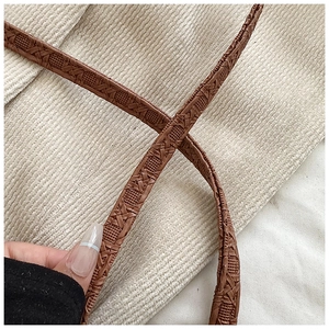 Detailed close-up of brown woven texture on a stylish shoulder strap with beige fabric backdrop