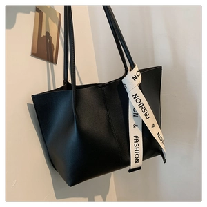 Detail of minimalist black tote bag with long strap and woven decorative fashion ribbon