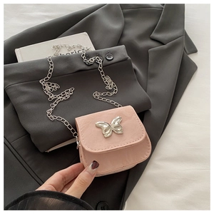 Detail van roze mini-tas met ketting en zilveren vlindergesp op een zwart jasje