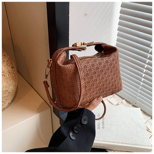 Detail of a brown woven texture handbag with metal buckle held by a model in soft light