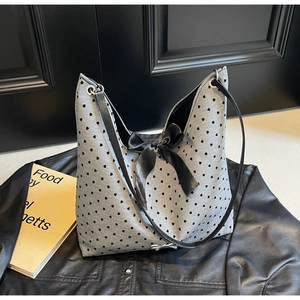 Detail of grey heart-pattern tote bag featuring a black satin bow and sleek shoulder strap