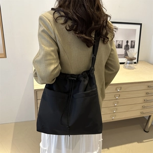 Minimalist black drawstring Oxford fabric tote bag worn as a shoulder crossbody messenger