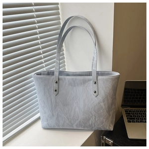 Detail of silver tote bag with pleated texture and metallic ring hardware in a chic office