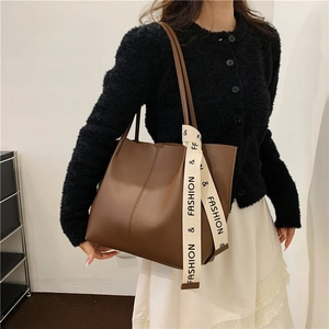 Brown faux leather tote bag with stylish logo ribbon detail shown on a model