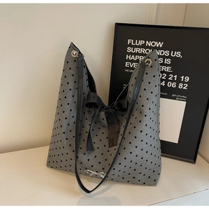 Close-up of grey heart-print tote bag featuring large black bow and silver metal charm