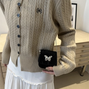 Mini zwarte crossbody tas met zilveren vlinder en kettingriem gedragen door een model