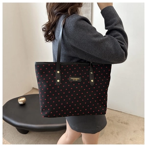 Detail of black tote bag with red heart pattern and leather strap with gold rivets