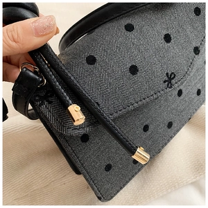Detail der grauen Tasche mit Fischgrätmuster, schwarzen Punkten und hochwertigem Ledergriff