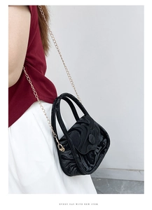 Detail of black crossbody bag with wave texture and gold chain strap on model