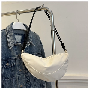 Detalle de un bolso media luna de nailon blanco colgado en un soporte con chaqueta vaquera