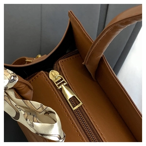 Détail du sac à main en cuir marron avec fermeture éclair dorée et foulard en soie élégant