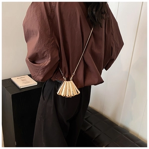 Detailed back view of a model wearing a golden shell-shaped crossbody bag with metal chain